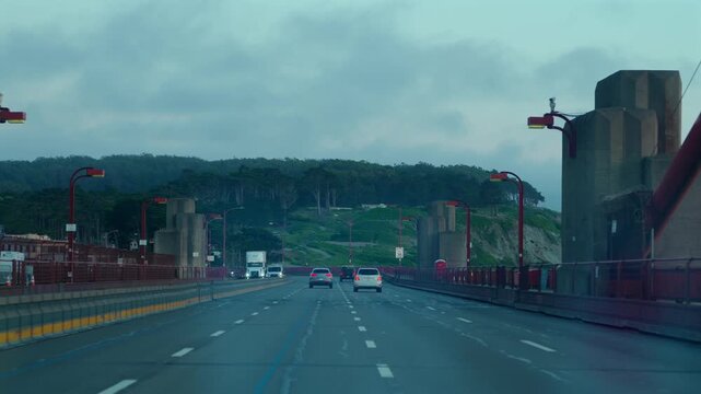 Point of view roadway scene with red bridge rails cables and low clouds
