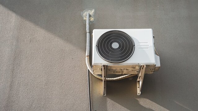 Outdoor air conditioner compressor unit mounted on concrete wall.