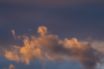 Fototapeta premium Vivid orange and gold cumulus clouds illuminated by sunset light against dark dramatic blue-grey sky