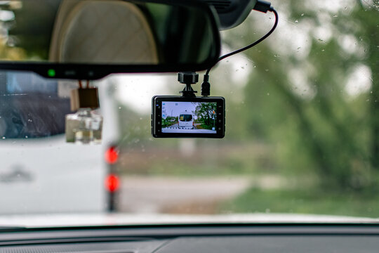 A windshield-mounted dashcam. The device is located under the rearview mirror. The LCD screen displays a real-time view of the road ahead. 