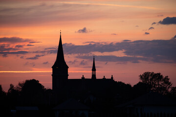 Naklejka premium A picturesque sunset over a quiet town, with the silhouette of a church silhouetted against a vibrant orange and pink sky.