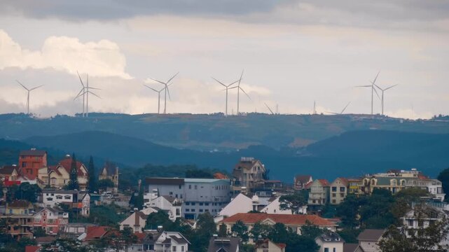 A scenic panoramic view of Da Lat &ndash; the City of Eternal Spring, Vietnam, highlighting the city's urban landscape nestled against the hills of Cau Dat wind farm with multiple wind turbines with rotatin