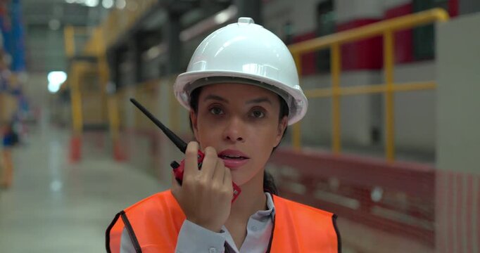 A female rail engineer wearing a hard hat and reflective vest inspects inventory, scans shelves, and reviews checklists in a large railway supply warehouse depot
