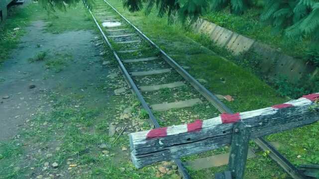 An old wooden bumper stop painted in red and white located at the end of a railroad track indicating a dead-end and the railway tracks stretching into the future
