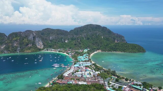 Phi Phi Island, Thailand : Aerial backward drone footage of jetty in Phi Phi Island with seafront resorts and limestone cliff and boat in the with dramatic sky in the Andaman sea in Krabi province.