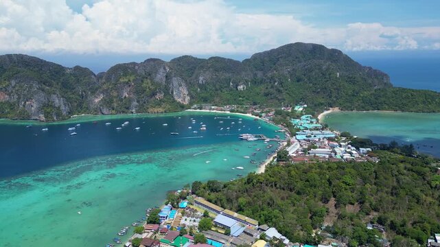 Phi Phi Island, Thailand : Aerial drone footage of jetty in Phi Phi Island with busy seafront resort surrounded by limestone cliff and many boats. Taken with tilt up motion