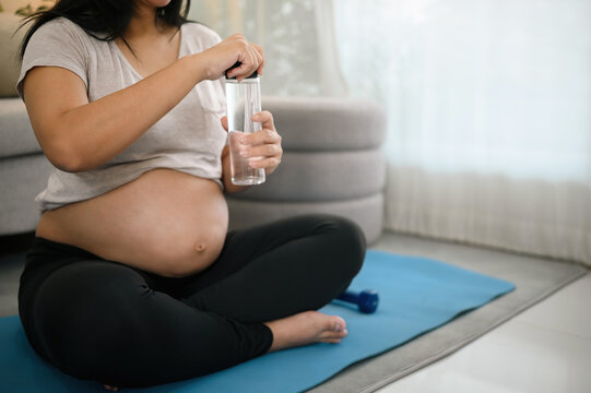 Pregnant Woman Sitting on Yoga Mat Holding Water Bottle During Home Workout Rest Break