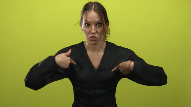 Young hispanic woman pointing to chest with both index fingers in lime green studio, open mouth and wide eyes; indignation disbelief.