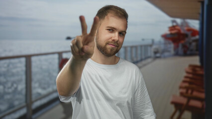 Fototapeta premium Man showing peace sign with hand on cruise ship deck building near railing and lifeboats; serene leisure travel.