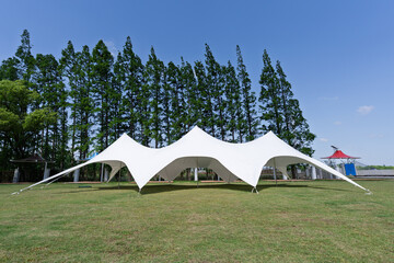 White Freeform Stretch Tent on Green Lawn with Pine Trees Blue Sky Outdoor Event Venue © Jin