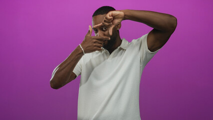 Naklejka premium Man framing face with fingers in posed studio against vibrant purple backdrop; creativity inspiration.