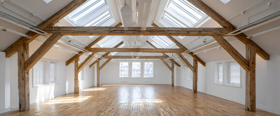 Fototapeta premium An expansive, empty interior features a gabled ceiling with exposed wooden beams, flooding the space with natural light. The floors are wooden