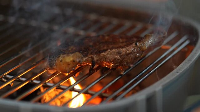 Grilled steak over hot flame on barbecue grill with smoke, charred crust and glowing fire, smoky meat dinner cooking close up outdoors on metal grate