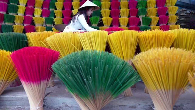 A young Vietnamese woman in a white national costume arranges colorful incense sticks in Hue, Vietnam.