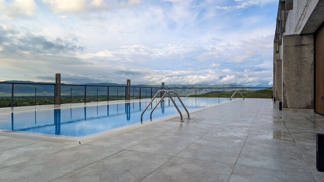 Rooftop infinity pool reflects a dramatic cloudy sky, elegant modern design and deck overlooking mountains and lush landscape for a serene luxury resort escape