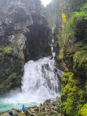 Waterfall cascades through rocky gorge surrounded by lush greenery on a misty afternoon © Tetiana