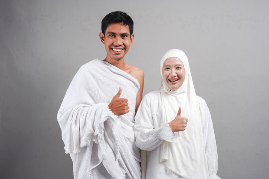 muslim pilgrims wife and husband wearing ihram and doing pointing upwards. over isolated by grey background. Hajj concept. concep islam muslim concept