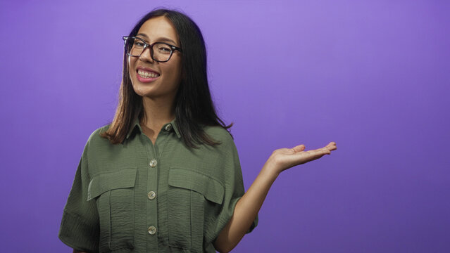 Young brunette woman holding out hand in studio with purple background; happiness confidence warmth.