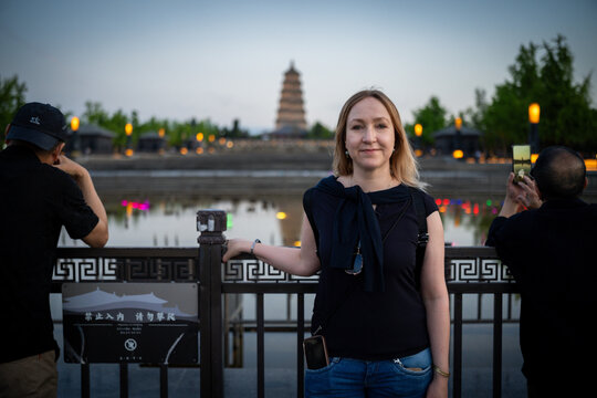 Woman smiling at camera with ancient pagoda and illuminated water in background