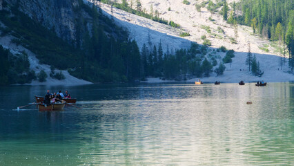 Rowers glide across a tranquil lake surrounded by towering mountains and lush greenery in a serene afternoon setting © Tetiana