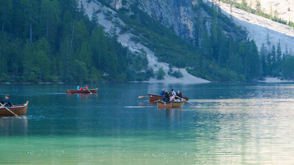 Rowers navigating serene waters at sunrise against a backdrop of lush forests and rocky cliffs in a tranquil lake setting © Tetiana