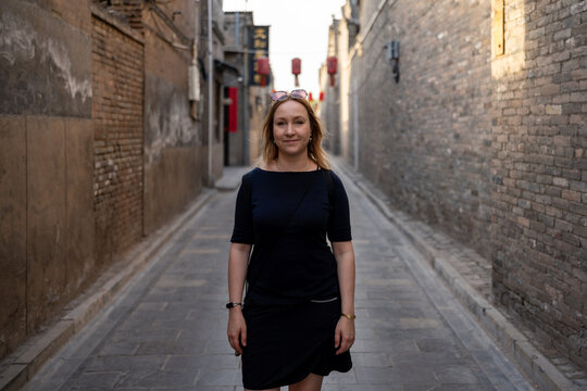 Woman walking down a narrow ancient street with brick buildings and red lanterns