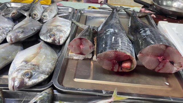 Close-up shot of fresh, gutted fish displayed at a market stall. The fish are arranged on stainless steel trays with sliced open bodies, showcasing the raw meat. 