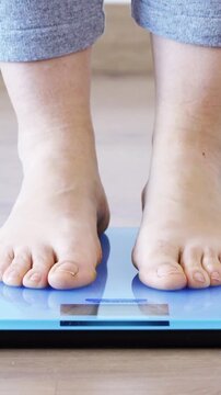 Closeup of a young woman weighing herself on a scale at home