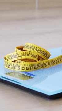 Closeup of a home scale and measuring tape thrown on the blue scale on a wooden floor.