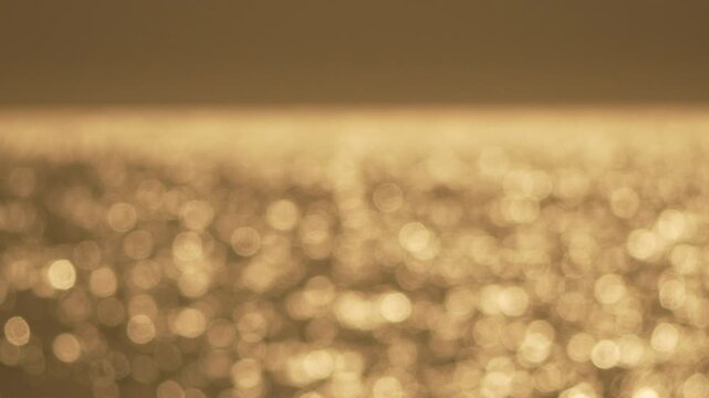 Bokeh water sunset golden sparkling light reflecting on ocean waves creating a dreamlike abstract background