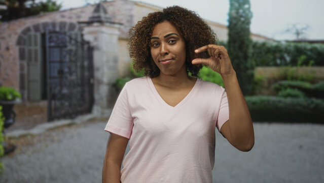 Woman holds fingers close in a small pinch gesture in front of a green building; playful measurement comparison.