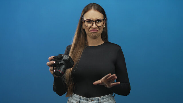 Woman holding dslr camera with raised hand and grimacing face showing disgust while checking lens in studio; disgust rejection.