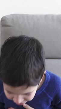Sneezing boy suffering from flu or allergy symptoms sitting on a sofa at home in winter