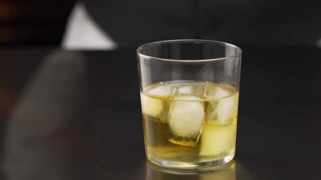 Bartender serving a cocktail in the glass with one big ice cube on the bar counter in the blurred