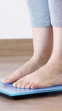 Close-up of a young woman weighing herself on a scale at home and throwing measuring tape on the blue scale.