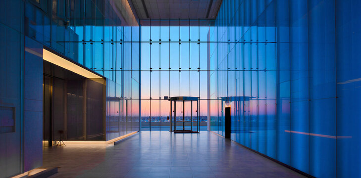 Modern corporate office lobby interior with floor to ceiling glass and panoramic view of sunset horizon at dusk with blue hour lighting real estate interior architecture twilight