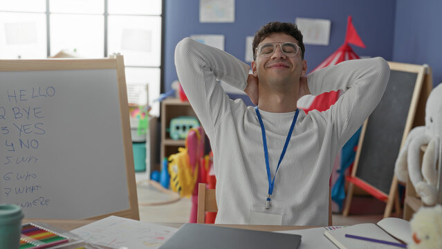 Man teacher gesturing with hands by laptop and whiteboard, then stretching hands behind head in classroom building; relaxed learning focus.
