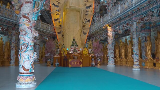 The large golden statue depicted is of the Bodhisattva Quan Am or Guan Yin (Avalokiteshvara), a central figure in Mahayana Buddhism surrounded by columns and balconies with intricate carvings, statues