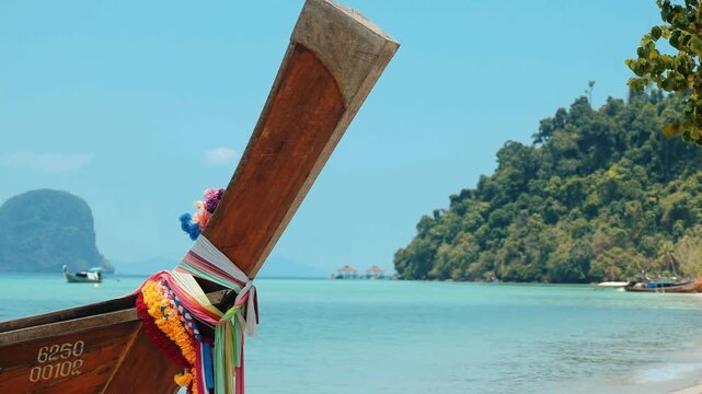 Wooden long-tail boat anchored near turquoise water shore, tropical island beach background with limestone karsts and green hills, summer vacation and Southeast Asia tourism
