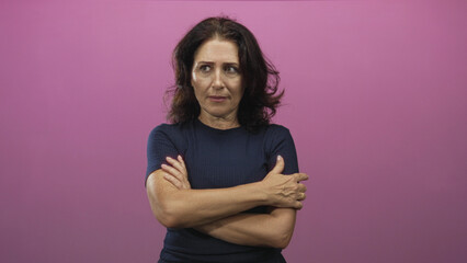 Obraz premium Middle aged woman arms crossed showing forearms and clasped hands against a pink studio backdrop, navy shirt; quiet contemplation.