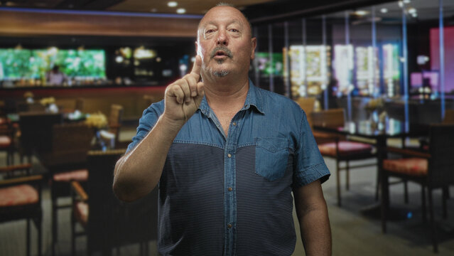 Man points finger at camera in a restaurant building, raising index finger in a clear pointing gesture; assertive warning.