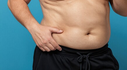Naklejka premium Man pinching belly fat on his stomach. Weight loss and obesity concept. Shirtless male body on blue background. Healthcare and diet theme