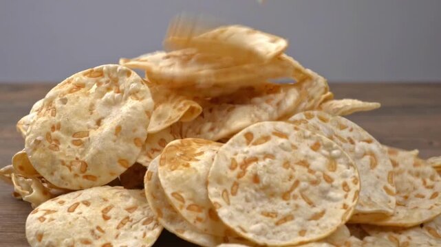Crispy tempeh chips falling onto a pile on a wooden table in a macro shot