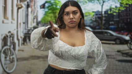 Fototapeta premium Woman pointing with hand on street in white lace blouse and black pants, shrugging in a dismissive pose; dismissal indifference.