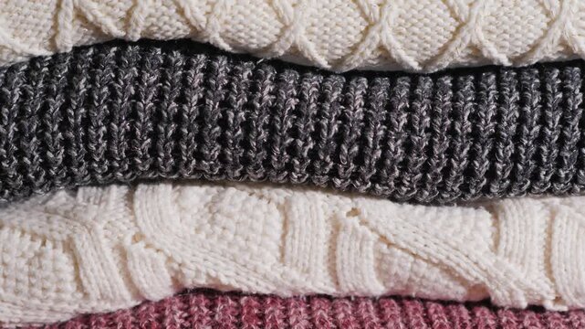 Stack of cozy knitted sweaters in neutral colors for winter warmth and comfort.