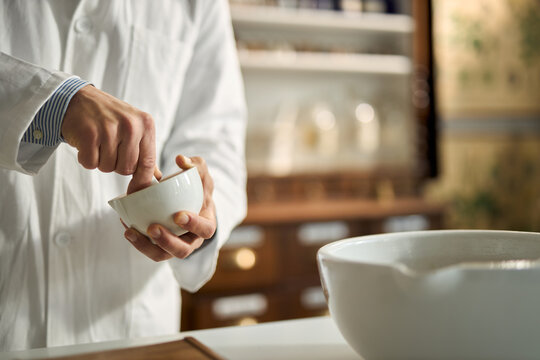 Close up of male scientist using mortar and pestle while making homeopathic medicine in laboratory.