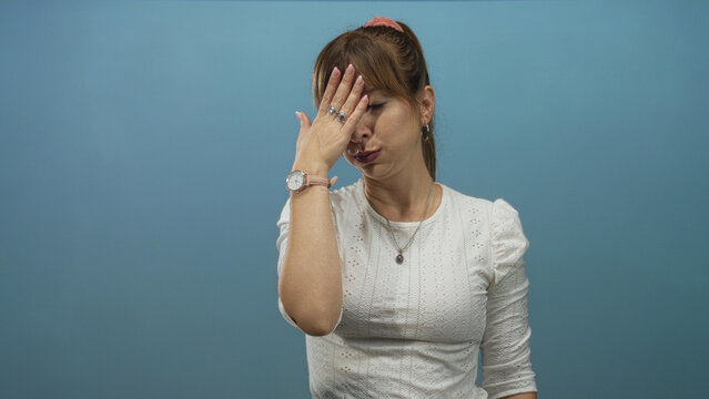 Woman in white blouse with hand covering face and wristwatch visible in blue studio, showing a facepalm gesture; frustration mistake.
