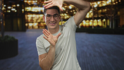 Fototapeta premium Man framing with hands and smiling in front of illuminated building at night; playful creativity inspiration.