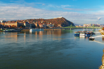 Fototapeta premium Panoramic view of the Danube river and historic city skyline in Budapest Hungary with sightseeing boats and green bridge under blue sky during autumn day