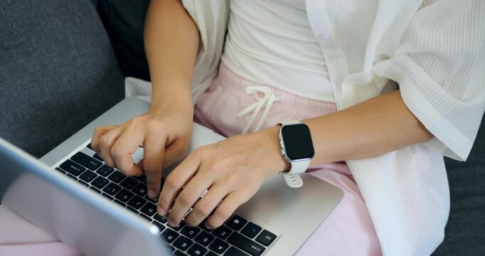 Person types while wearing smartwatch. Individual focuses on typing in quiet environment. Person diligently edits documents at home while monitoring time with smartwatch during calm work period